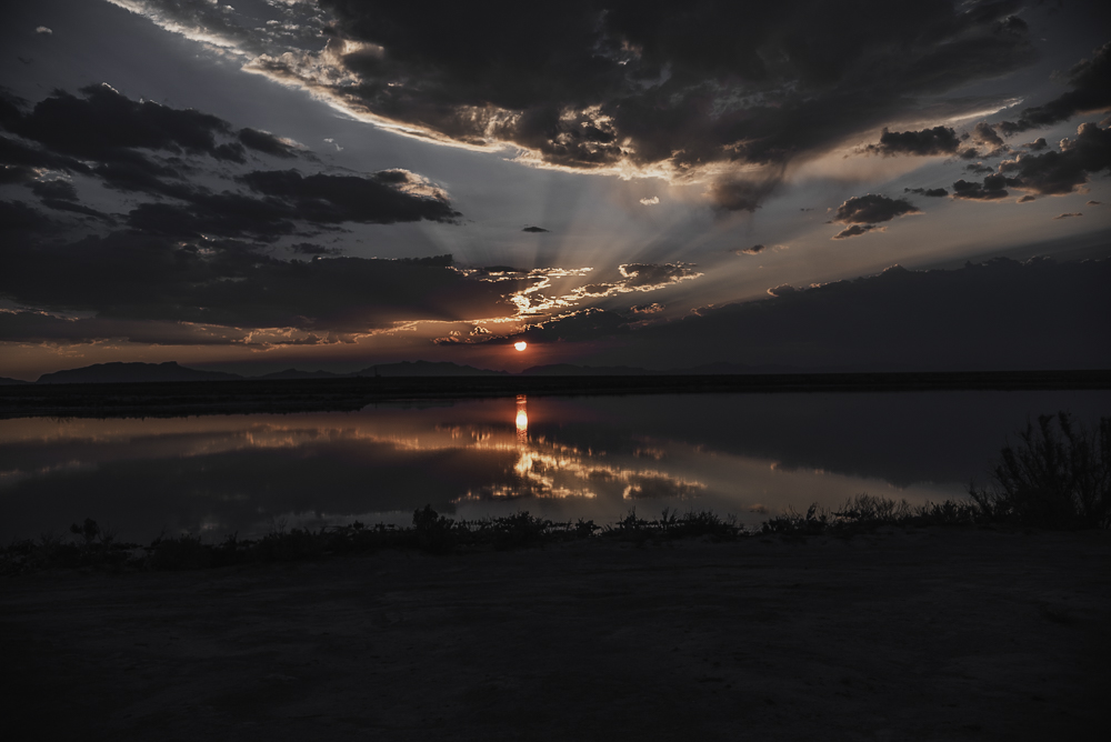 Dark clouds and a red sunset reflected on still desert water photographed by Rory Duffy