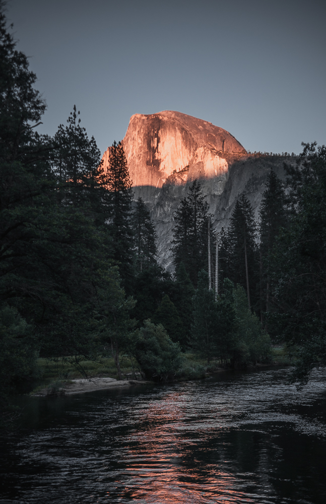 Half Dome glowing above a dark forest and river at sunset photographed by Rory Duffy