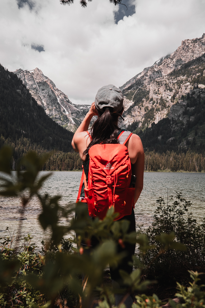 Hiker with a red backpack overlooking a mountain lake photographed by Rory Duffy