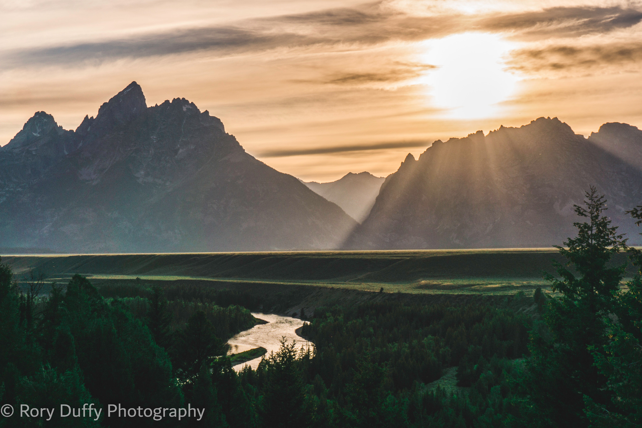 Sunbeams breaking across the Teton Range and winding river photographed by Rory Duffy